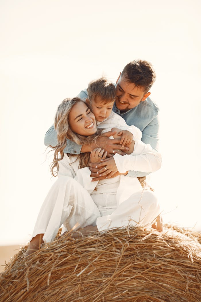 A joyful family enjoying a sunny day outdoors, sitting on a hay bale.