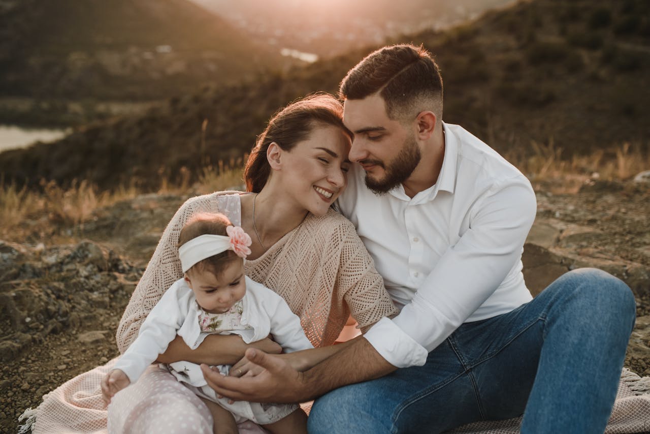A joyful family sitting together outdoors during sunset, bonding with their baby.