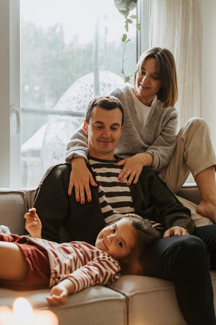 A joyful family bonding moment on the couch with parents and child enjoying a cozy day indoors.